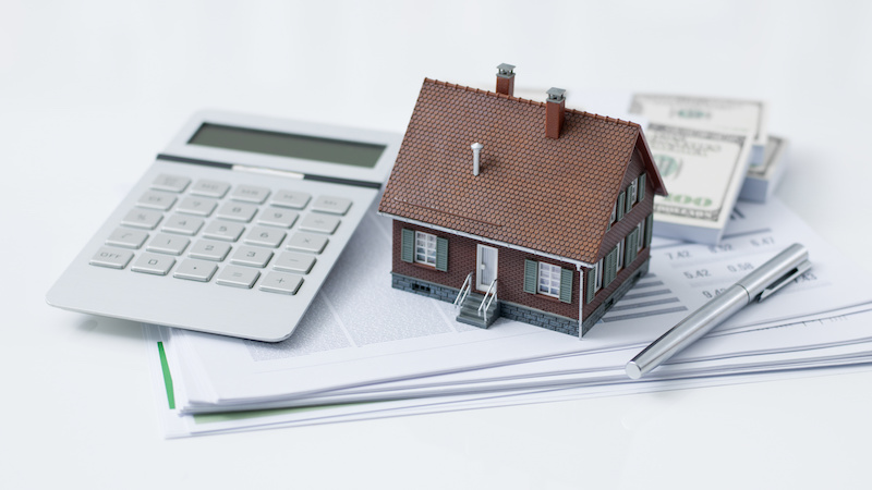 Model house, calculator, cash money and paperwork on a desk: real estate, home loan and investments concept